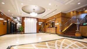 Vestíbulo de hotel con piso de mármol pulido, mostrador de recepción, una escalera y una lámpara de araña grande.