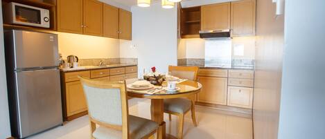 A modern kitchen with wooden cabinets, a stainless steel refrigerator, a microwave, and a dining table with chairs.