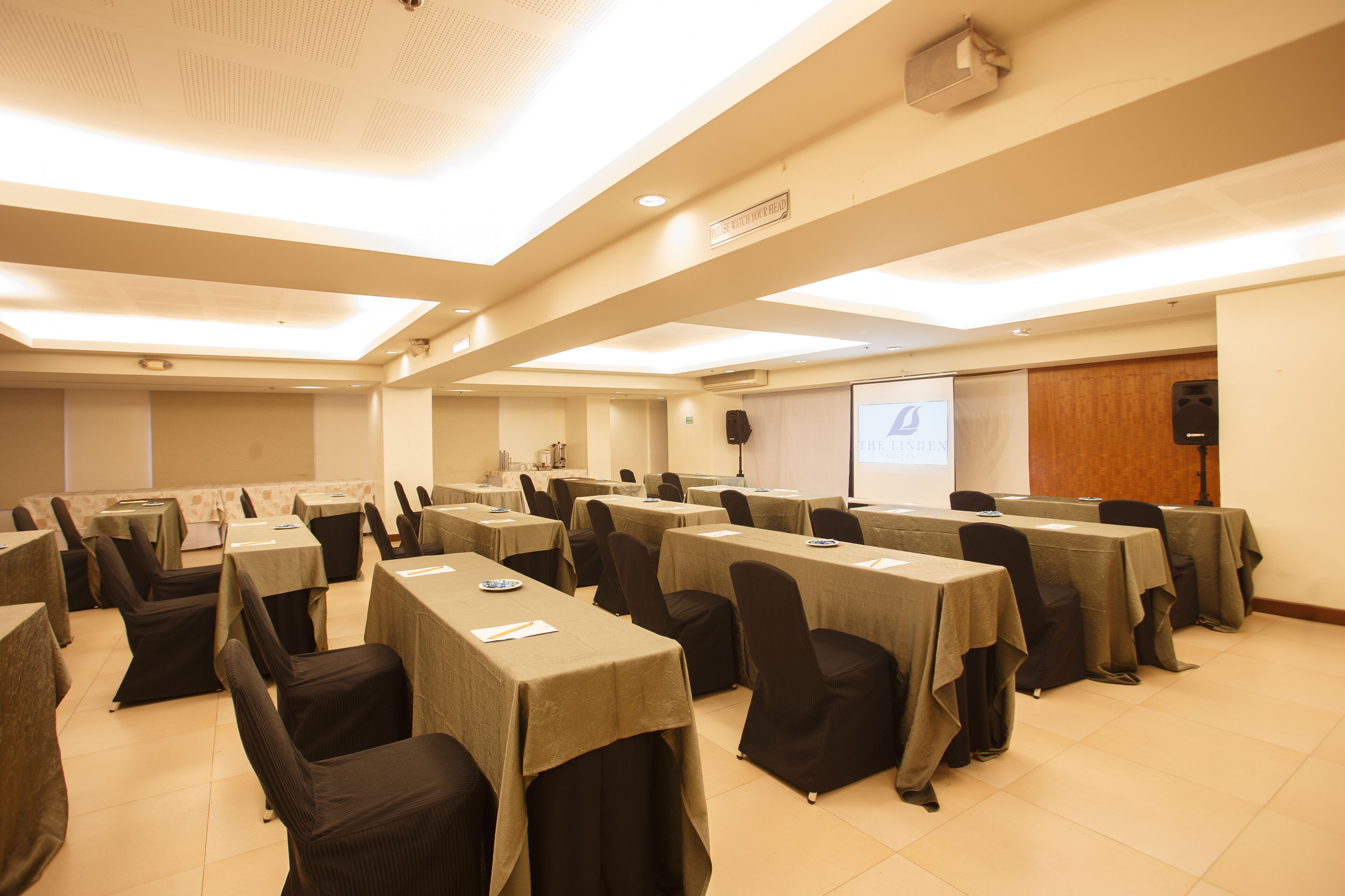 A conference room with multiple tables and chairs, equipped with projectors and a screen.