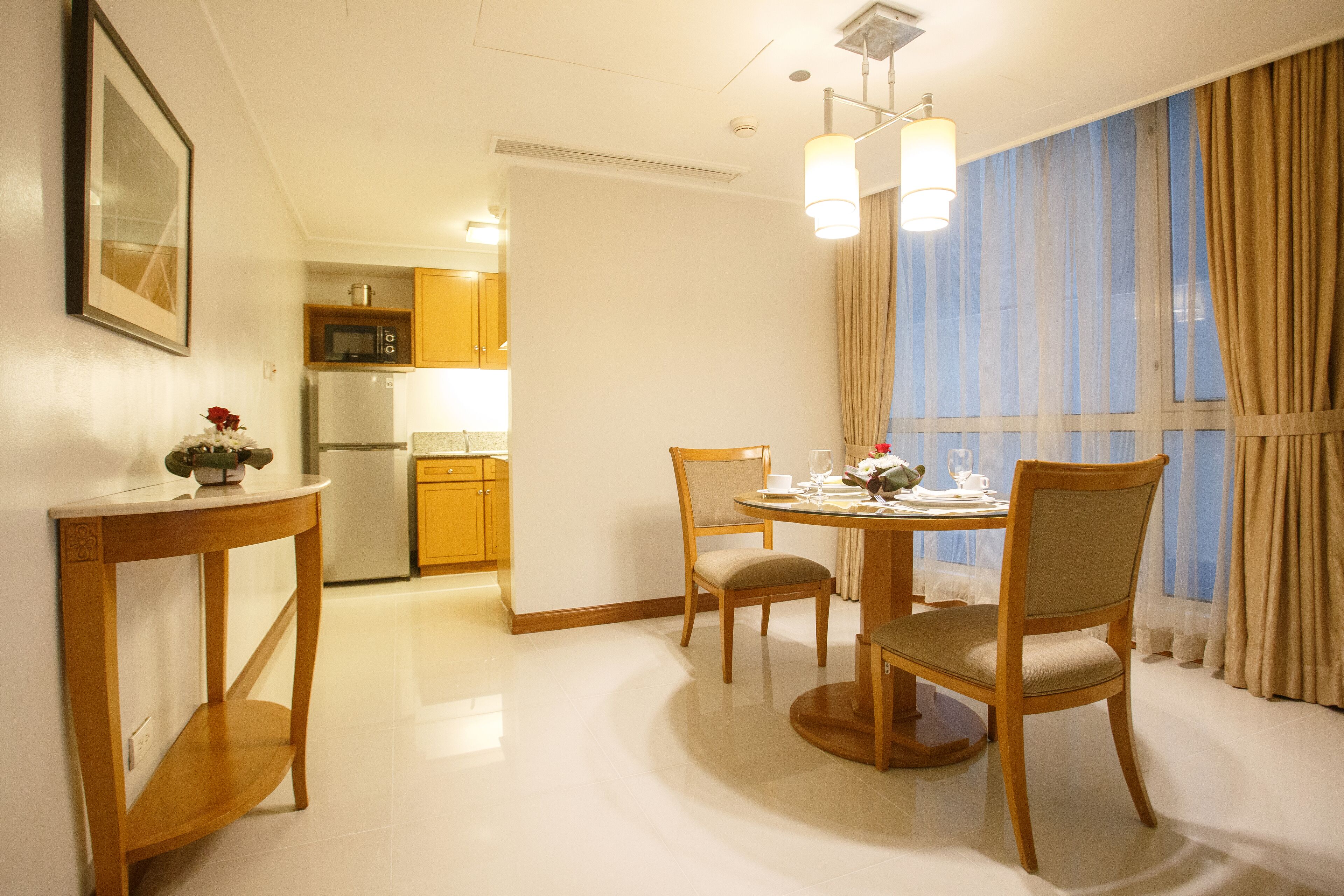 Un coin repas avec une table dressée pour deux personnes, une chaise et une petite table sur laquelle est posé un vase.