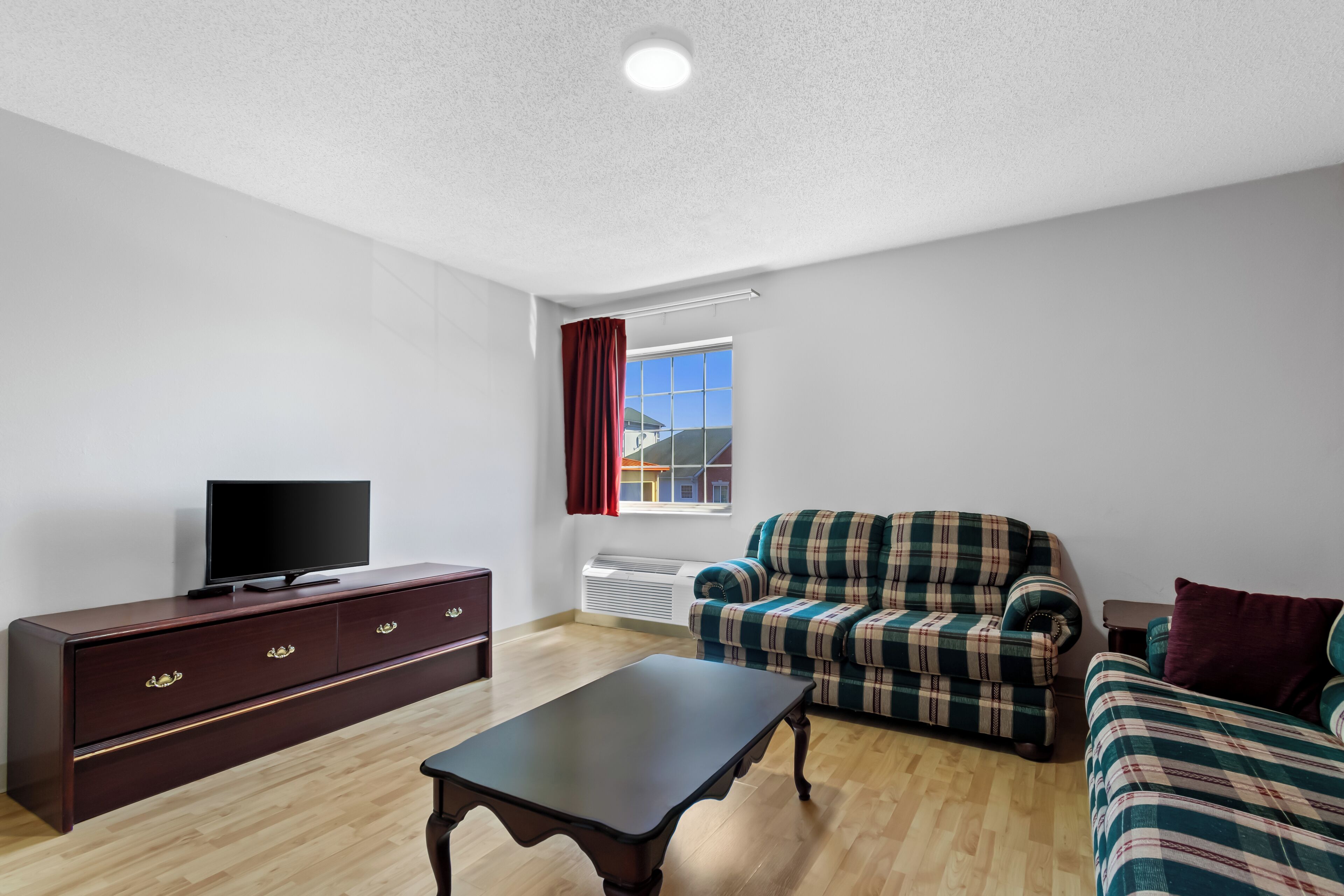 A living room with a dark wooden TV stand, a plaid sofa, a matching armchair, and a small table.