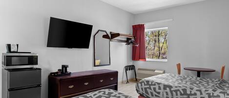 A hotel room with a bed, a desk, a TV, a microwave, and a dresser.