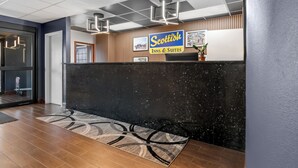 En reception med en svart disk, en skylt med texten ”Scottish Inns & Suites” och en väggpanel av trä med inramade bilder.