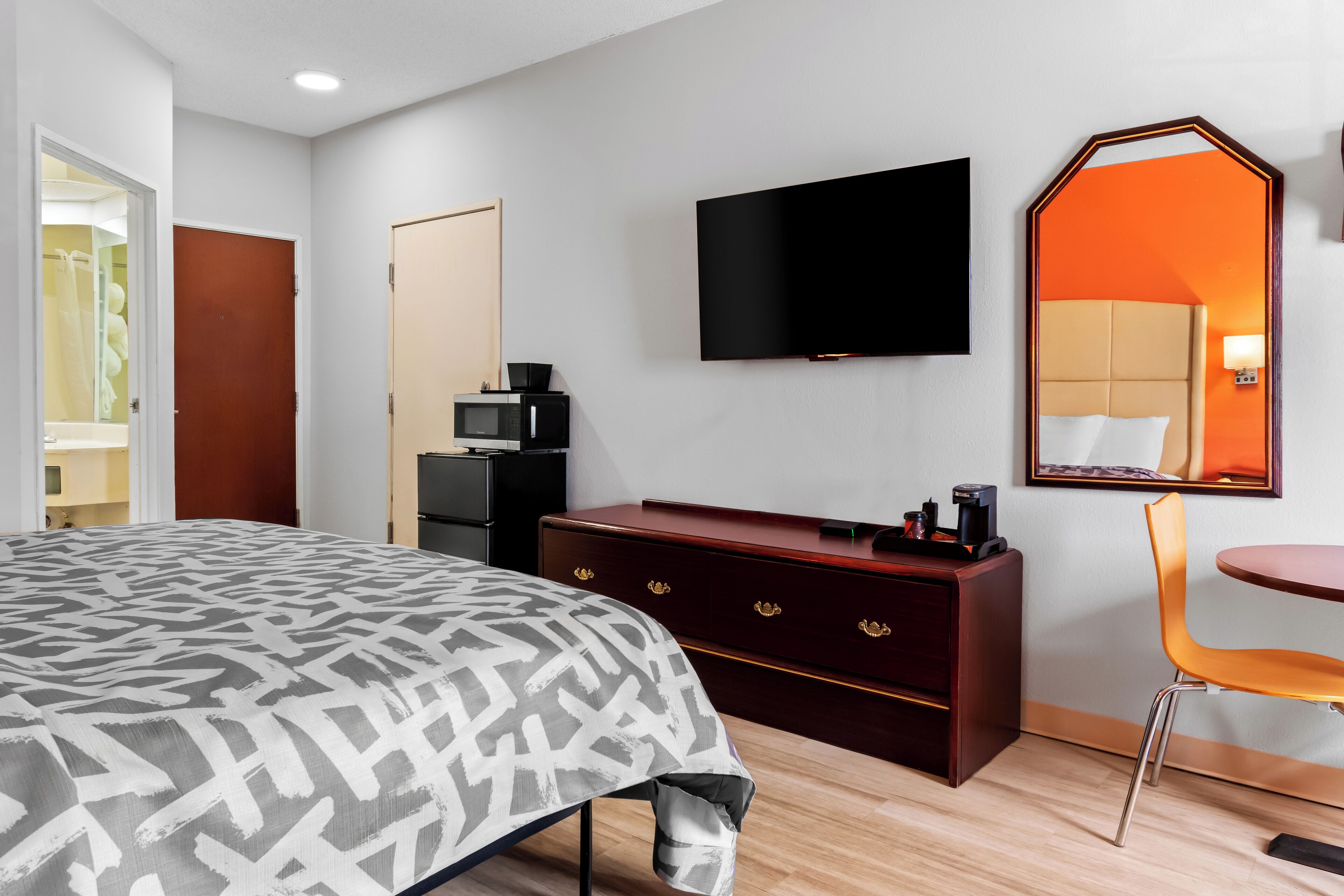 Una habitación de hotel con una cama, televisión, cómoda, silla y espejo.