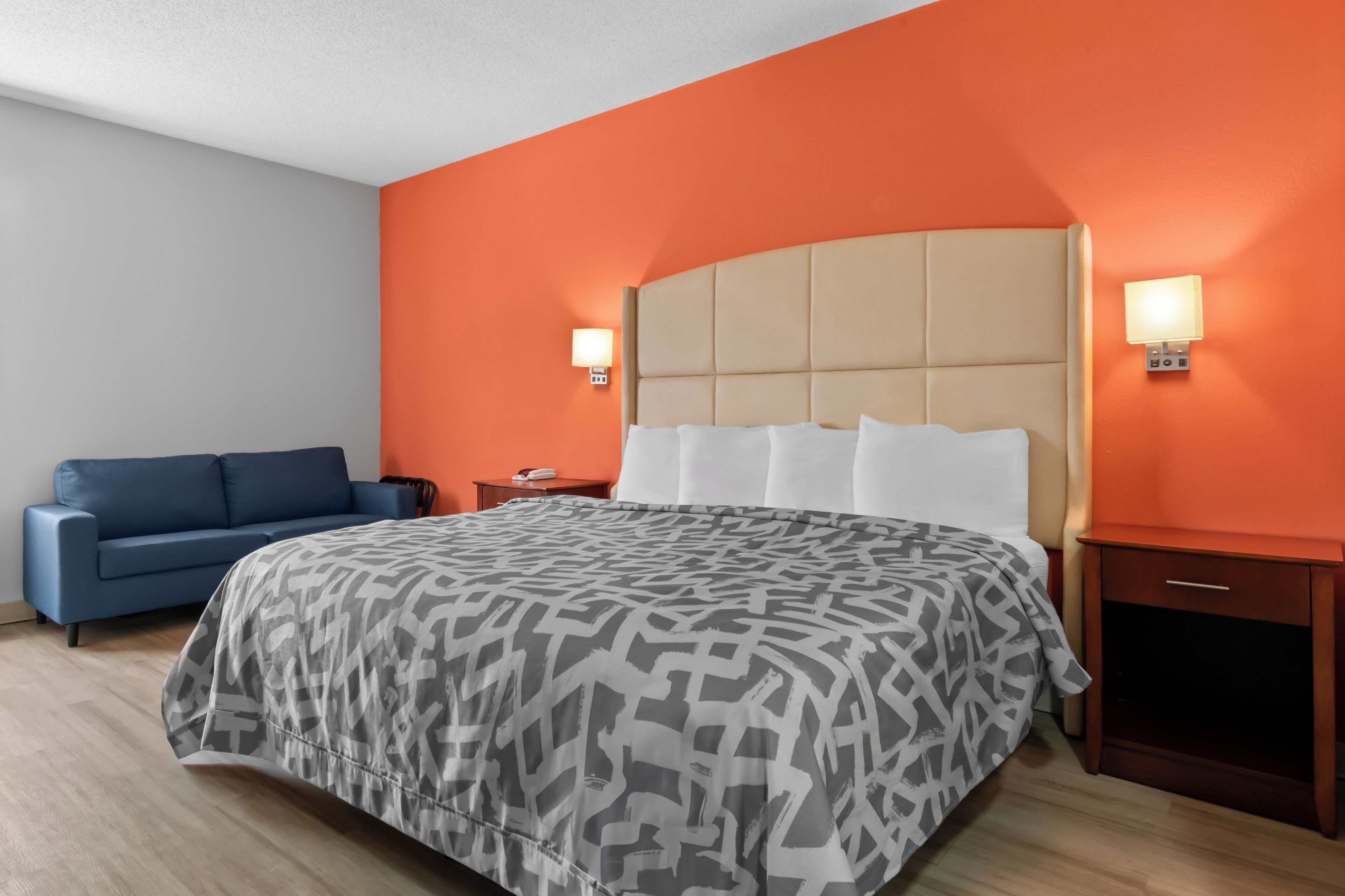 A hotel room with a large bed, a blue sofa, two bedside tables, and orange walls.