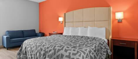 Une chambre d’hôtel avec un grand lit, un canapé bleu, deux tables de chevet et des murs orange.