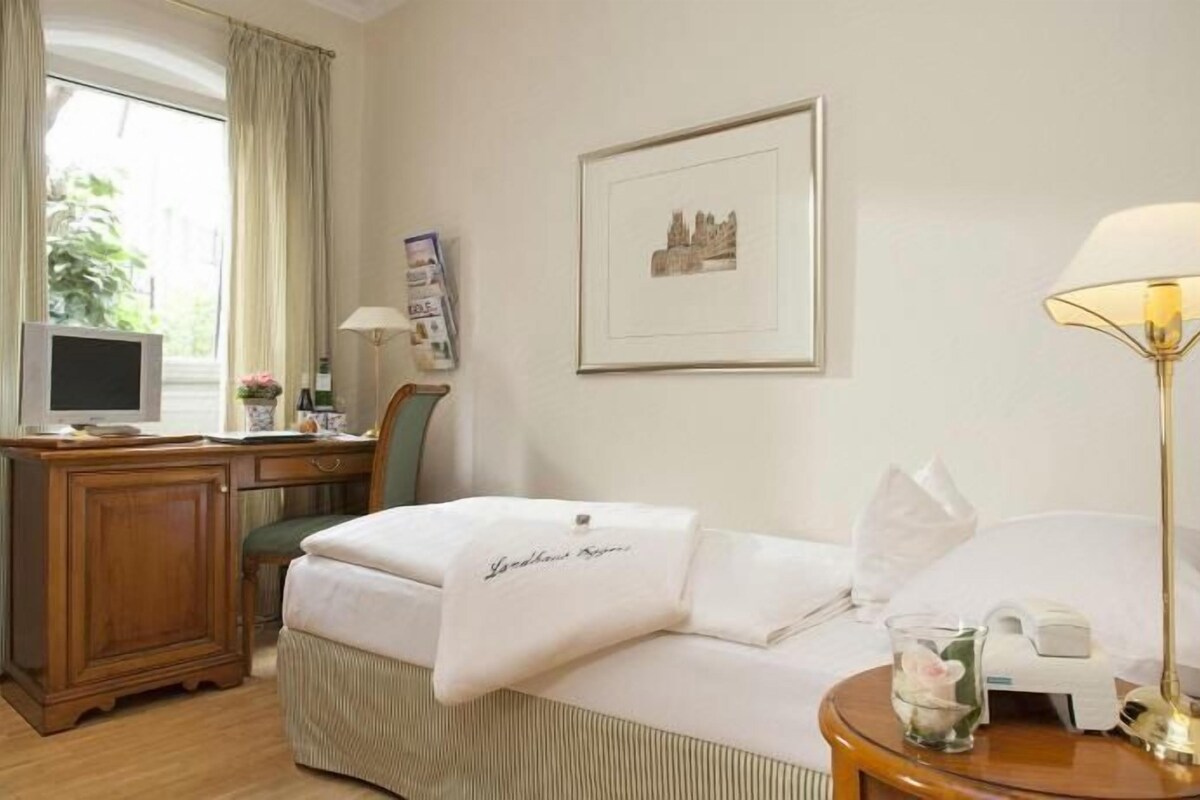 A hotel room with a bed, desk, chair, lamp, and a window with curtains.