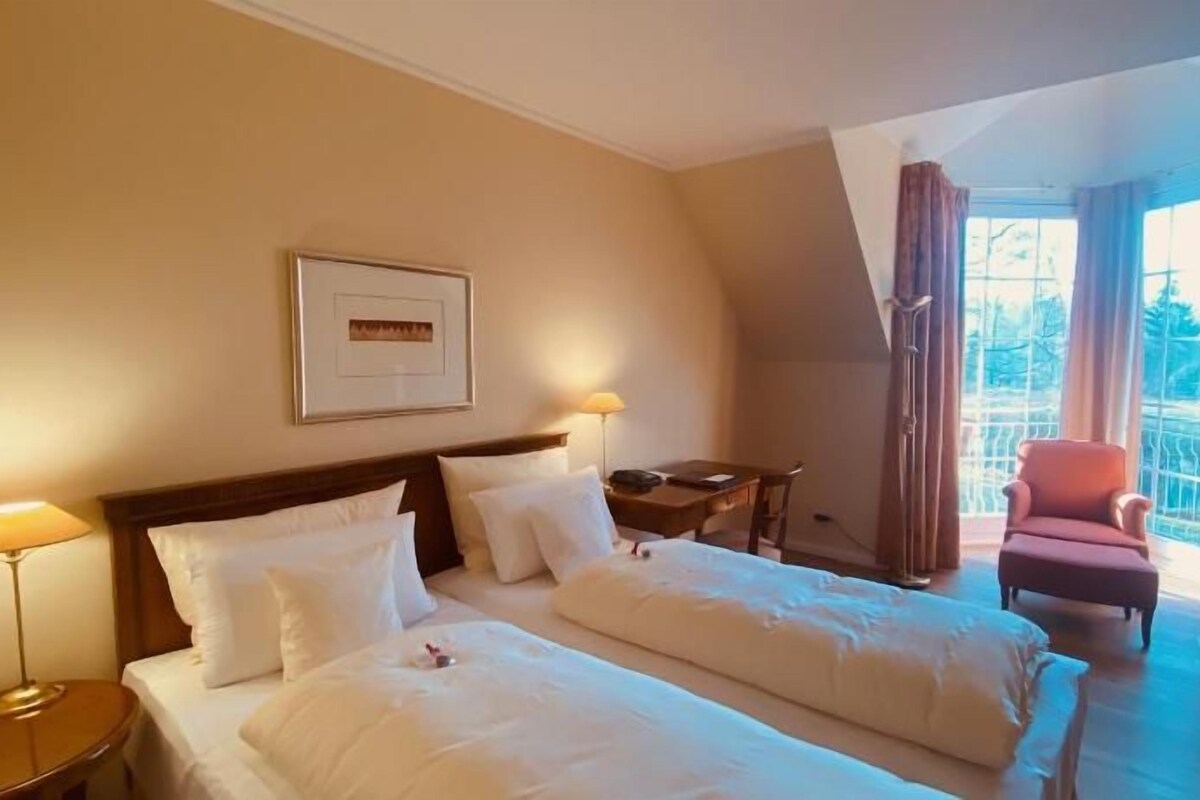 A hotel room with two beds, a desk, a chair, and a large window with curtains.