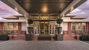 Entrada de hotel con diseño moderno, que presenta fachada de ladrillo, puertas de cristal amplias y un corredor cubierto.