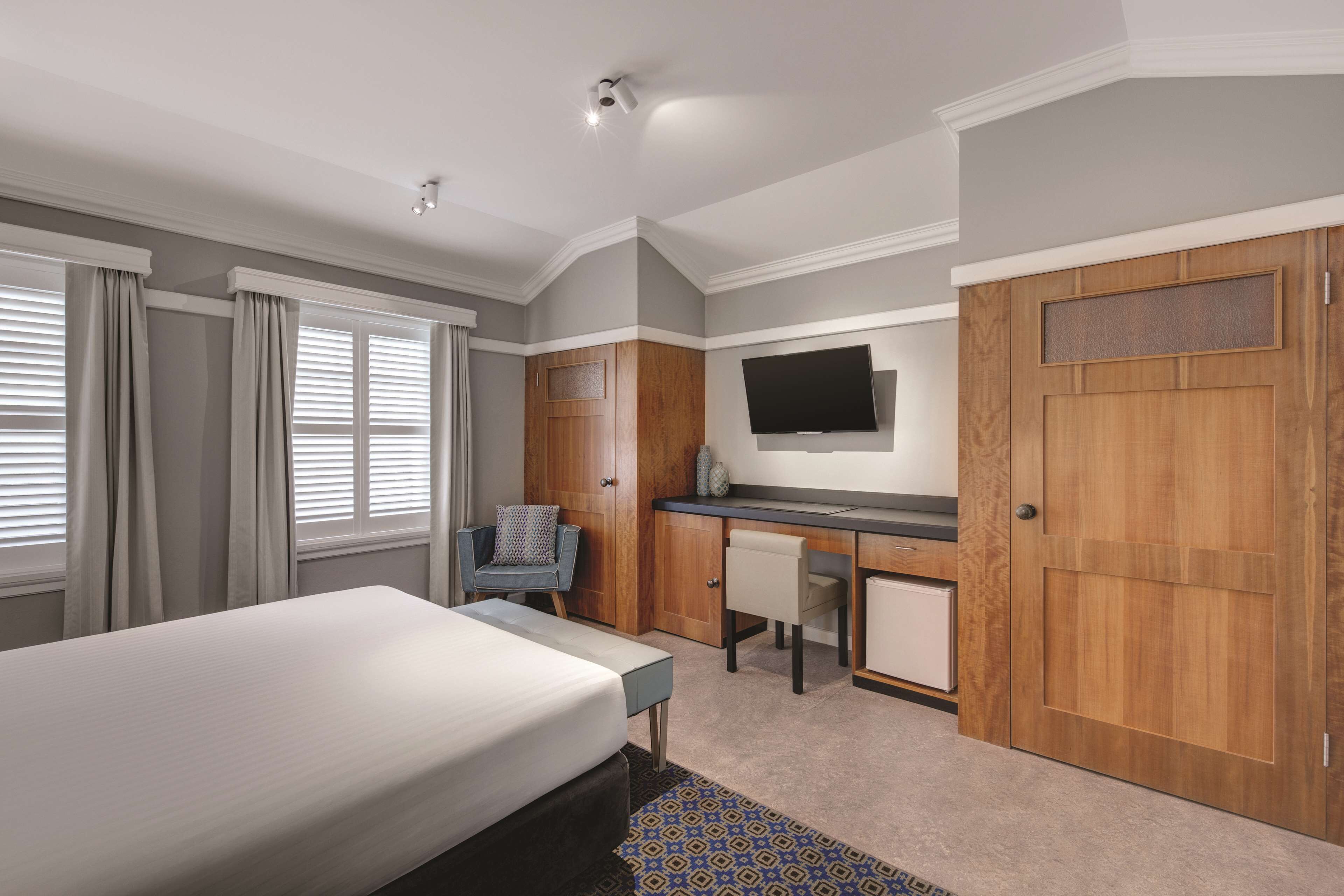 A hotel room with a bed, desk, chair, TV, and wardrobe.