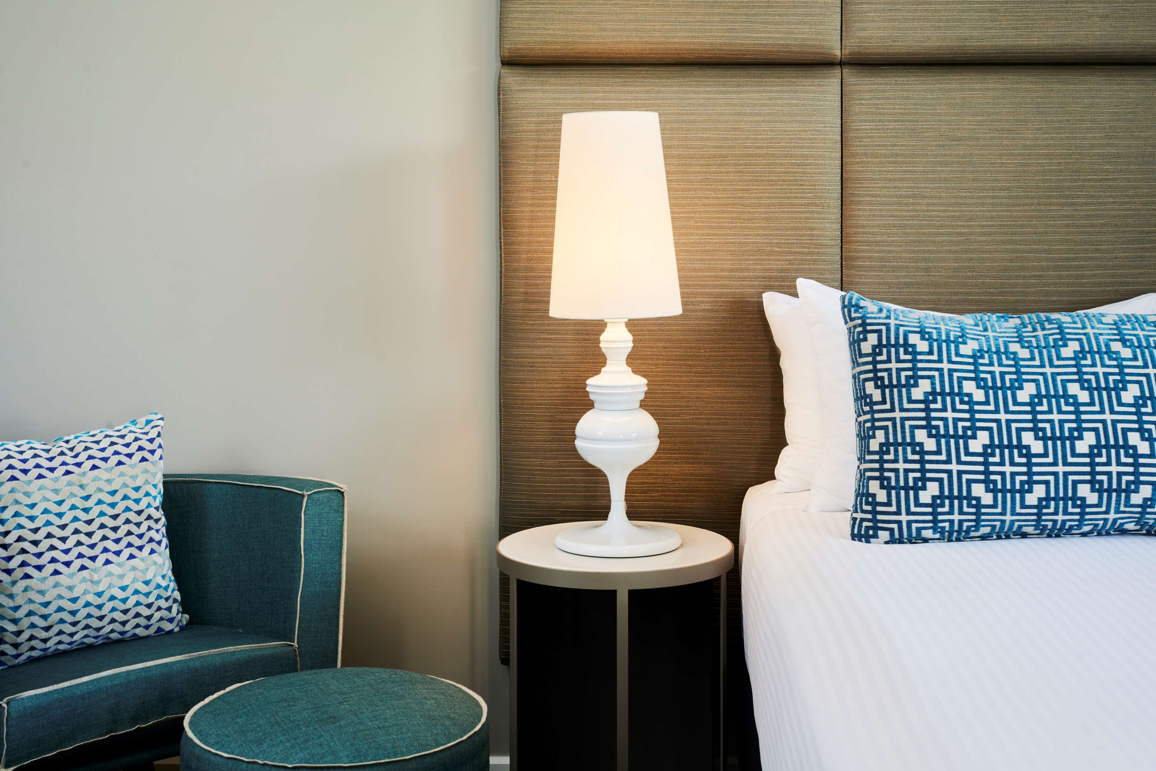 Una camera d'albergo ordinata con un letto, un tavolino con una lampada, un divano e cuscini decorati.