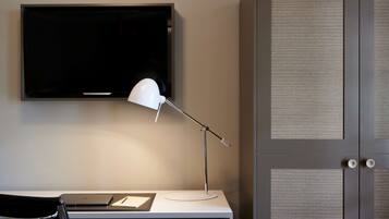 A modern room with a flat-screen TV mounted on the wall, a white desk with a lamp, and a closed door with a textured panel.