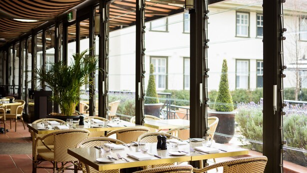 Un restaurante con terraza, ventanas amplias y plantas en macetas.