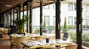 A restaurant with outdoor seating, large windows, and potted plants. - Hotel Kurrajong Canberra (Barton)