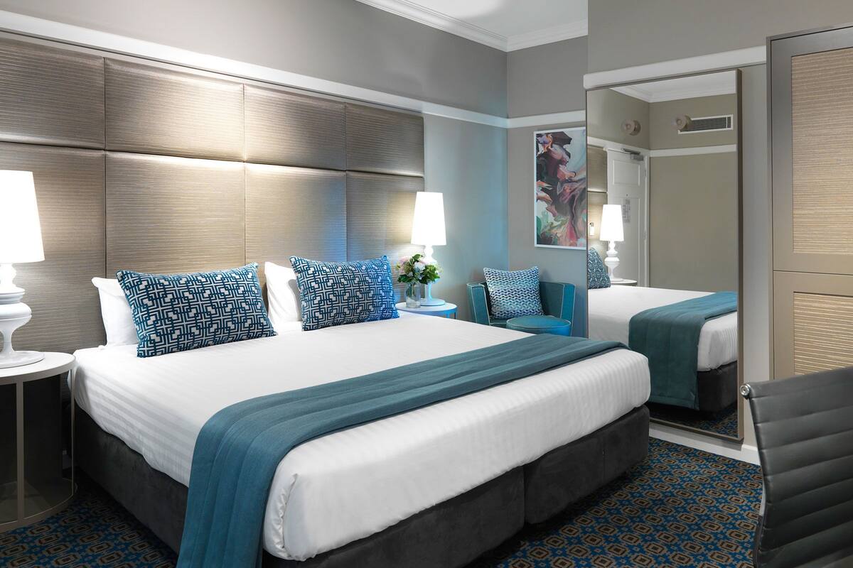 A hotel room with a large bed, a smaller bed, a desk, and a chair.