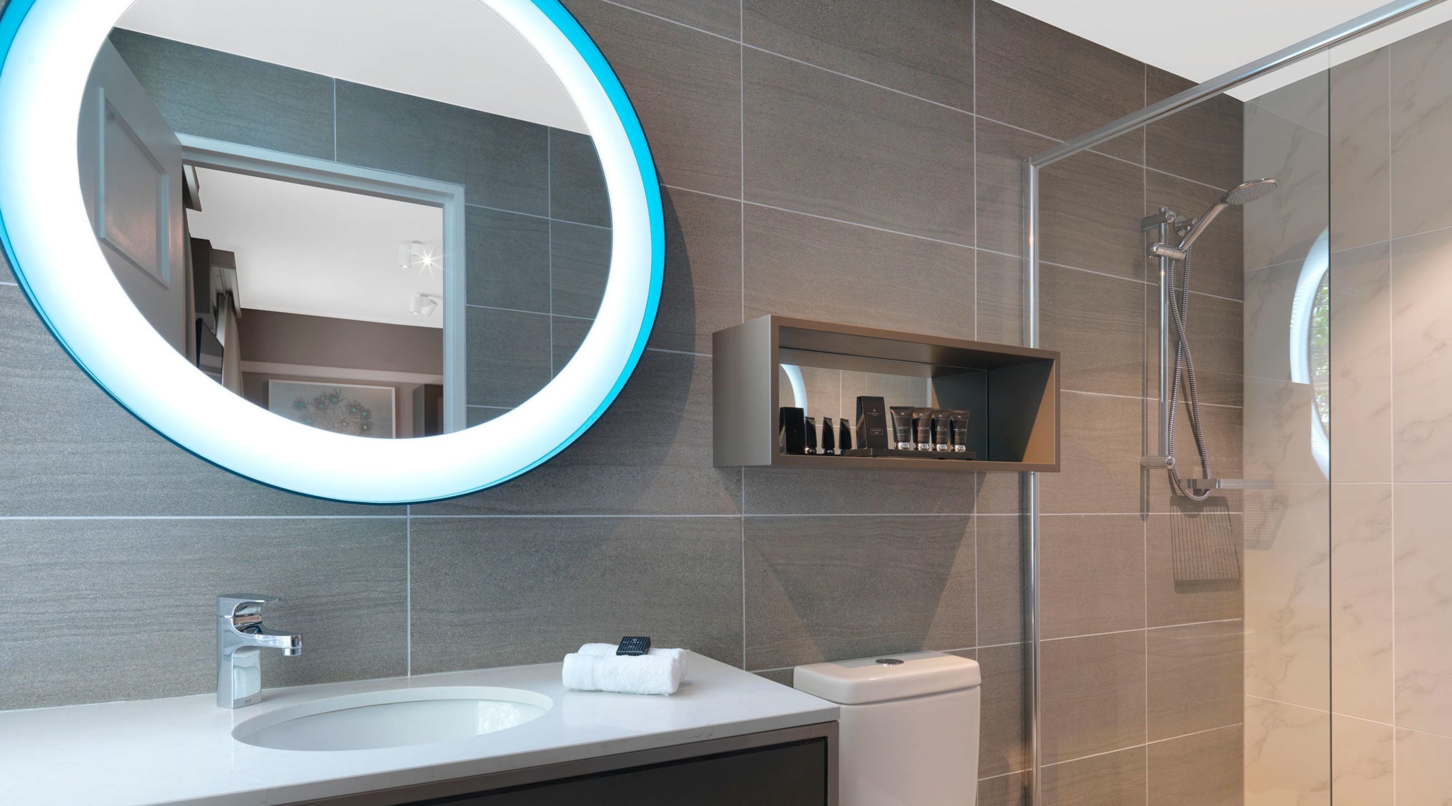 A modern bathroom with a large mirror, a sink, a toilet, and a shower area.