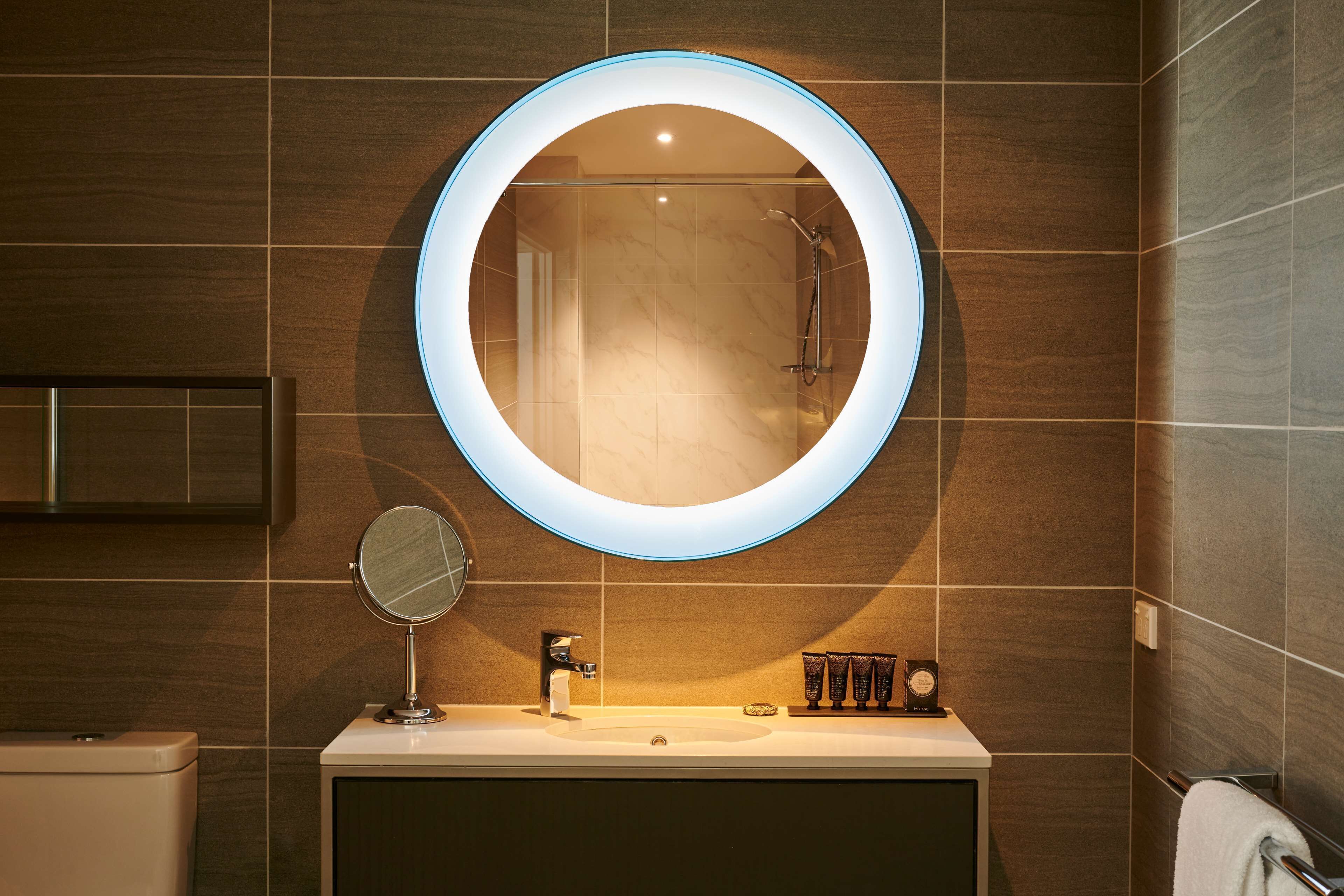 A modern bathroom with a round mirror, a handheld mirror, a sink, and a shower.