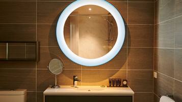A modern bathroom with a round mirror, a handheld mirror, a sink, and a shower.