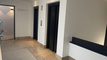 Un pasillo con dos ascensores negros, un cartel que indica los números de habitación 501 al 507, y una alfombra texturizada.