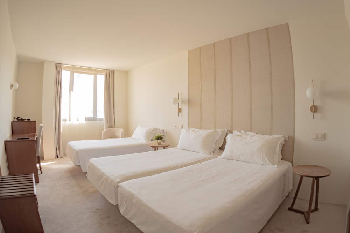 A hotel room with two beds, a desk, a chair, a small table, and a window with curtains.