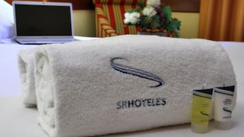 A neatly folded white towel with embroidered text and a logo, accompanied by two bottles of shampoo and conditioner.