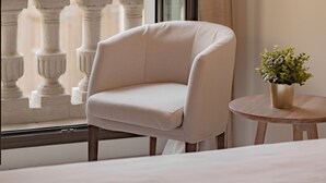 A hotel room with a balcony, a white armchair, a small round table with a plant, and a view of a building with classical architecture. - Hotel Oriente (Zaragoza)