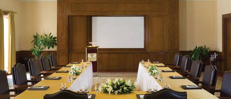 Un salón de conferencias con una larga mesa, sillas, una pantalla de proyector y un atril.