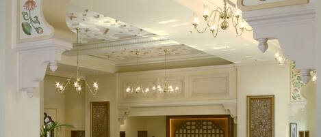 A lobby with a checkered floor, seating area, chandeliers, and floral wall decorations.