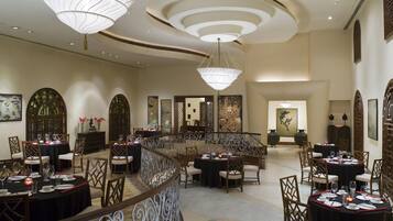 A spacious dining area with multiple round tables, elegant chandeliers, and traditional decor.