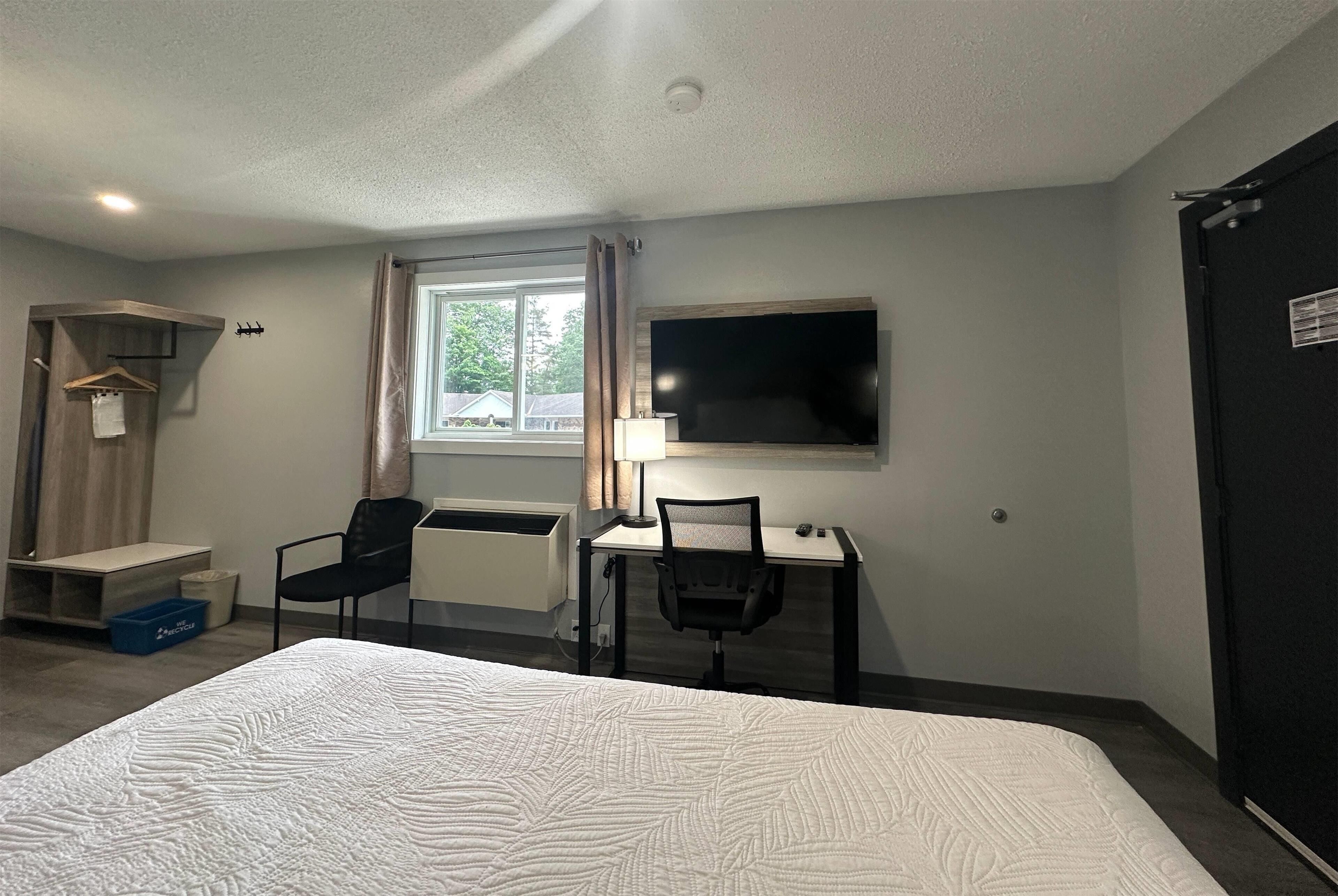 A hotel room with a bed, a desk with a chair, a TV, and a wardrobe.