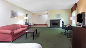 Een hotelkamer met een bed, een rode bank, een bureau met een computer, een televisie en een open haard.