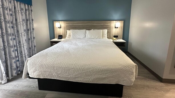 Een hotelkamer met een groot bed, twee nachtkastjes en een hoofdbord met wandlampen.