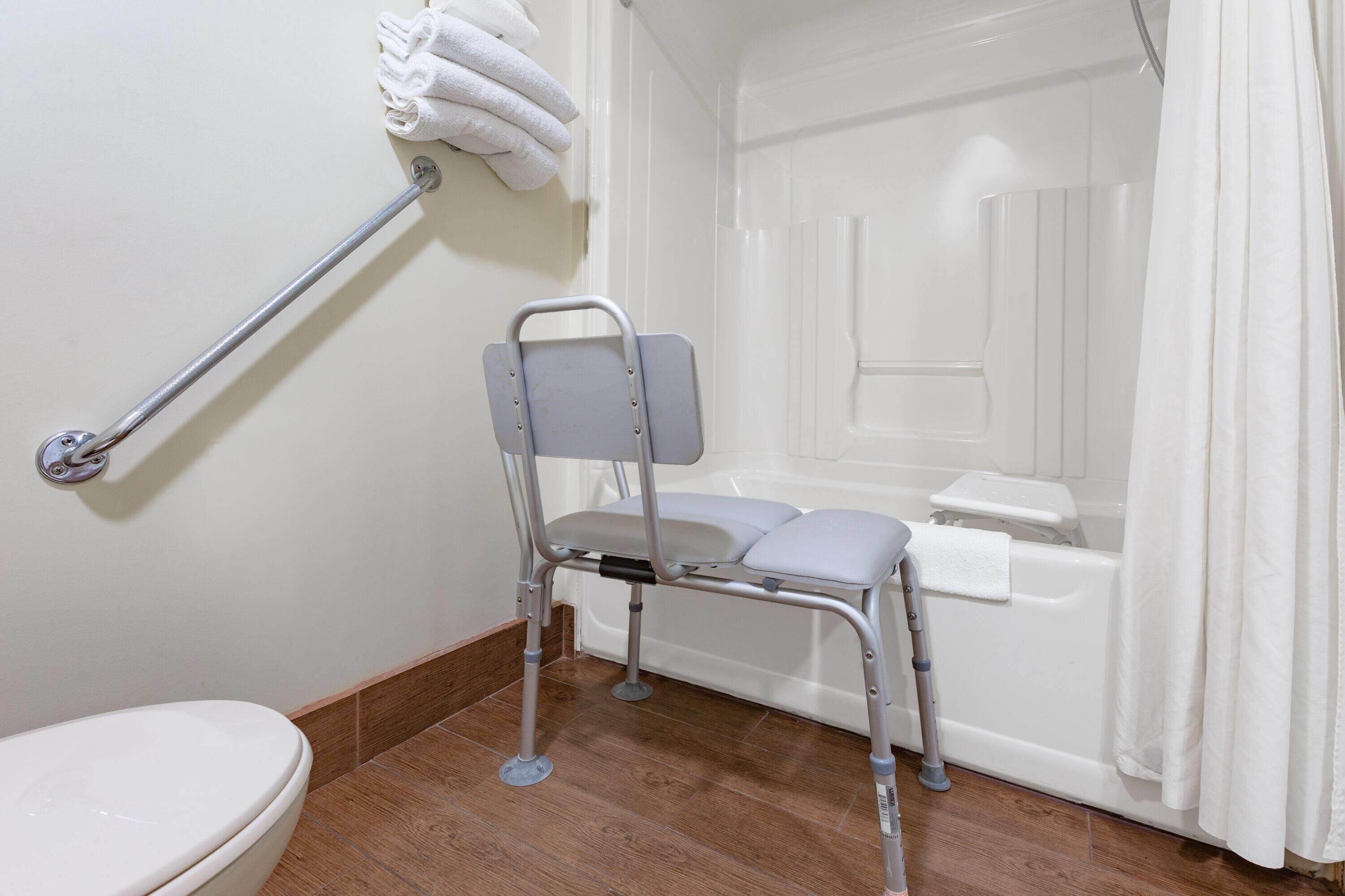 Un baño con ducha accesible en silla de ruedas, barra de apoyo y bañera blanca.