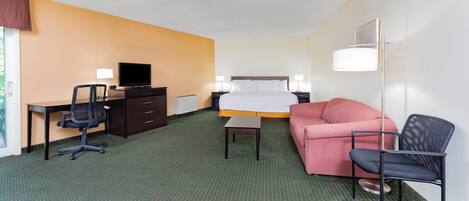 A hotel room with a bed, a desk with a chair, a sofa, a TV, and a floor lamp.