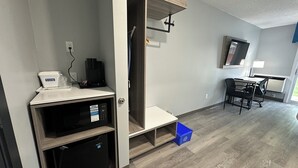 Een moderne, goed verlichte kamer met een kitchenette, een bureau en een stoel, en een aan de muur bevestigde televisie.