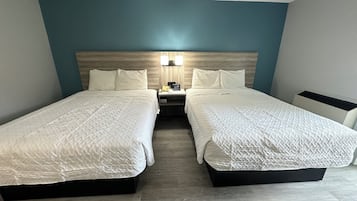 Une chambre d’hôtel avec deux lits, une table de chevet, une lampe et une tête de lit en bois.