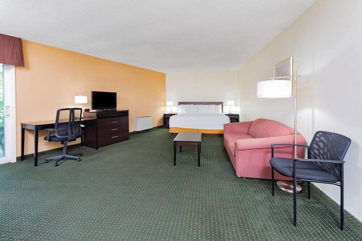 Habitació d'hotel amb un llit, una taula de treball amb una cadira, un sofà, un televisor i una làmpada.