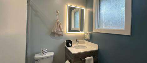 A bathroom with a toilet, sink, vanity, and a mirror with built-in lighting.