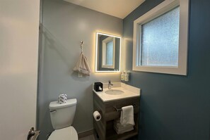 A bathroom with a toilet, sink, vanity, and a mirror with built-in lighting. - Travelodge by Wyndham Bracebridge (Bracebridge)