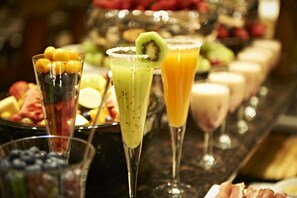 Un buffet proposant une variété de plats et de boissons, notamment un smoothie vert agrémenté d’une tranche de kiwi et un verre de jus d’orange.