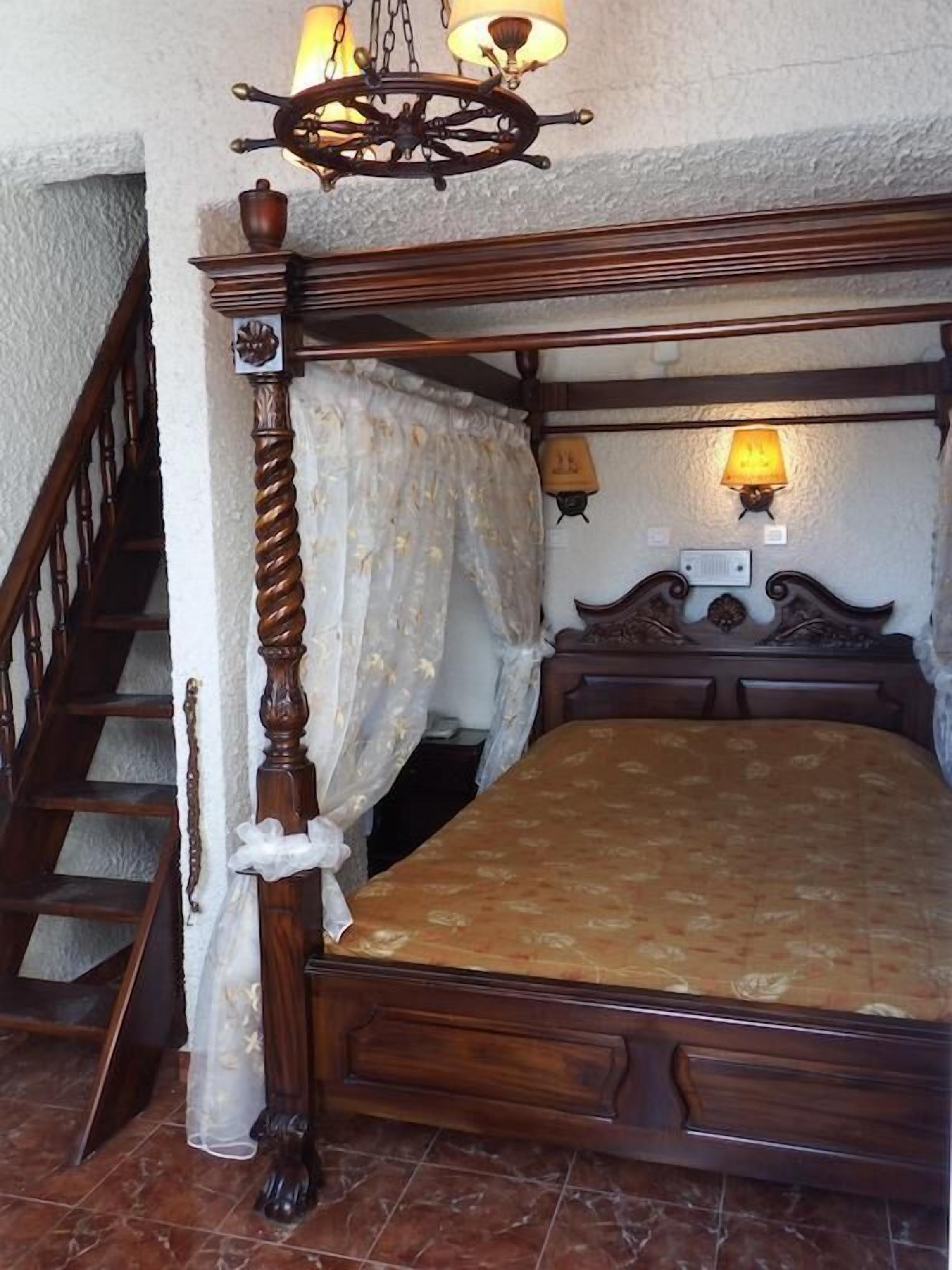 Un lit à baldaquin en bois, avec quatre poteaux, un escalier en bois et deux lampes fixées au mur.
