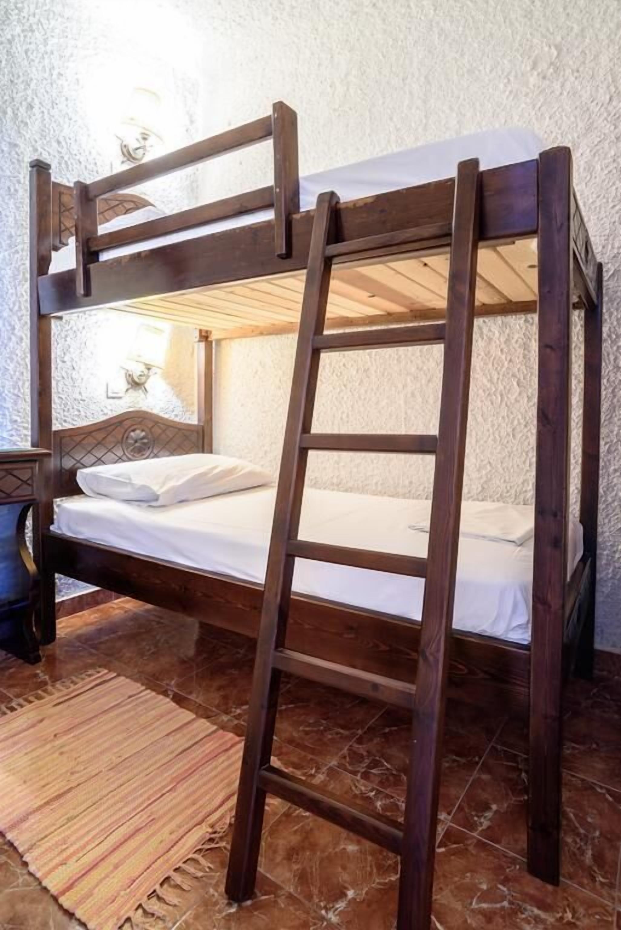A bunk bed with a wooden ladder, white bedding, and a textured wall.