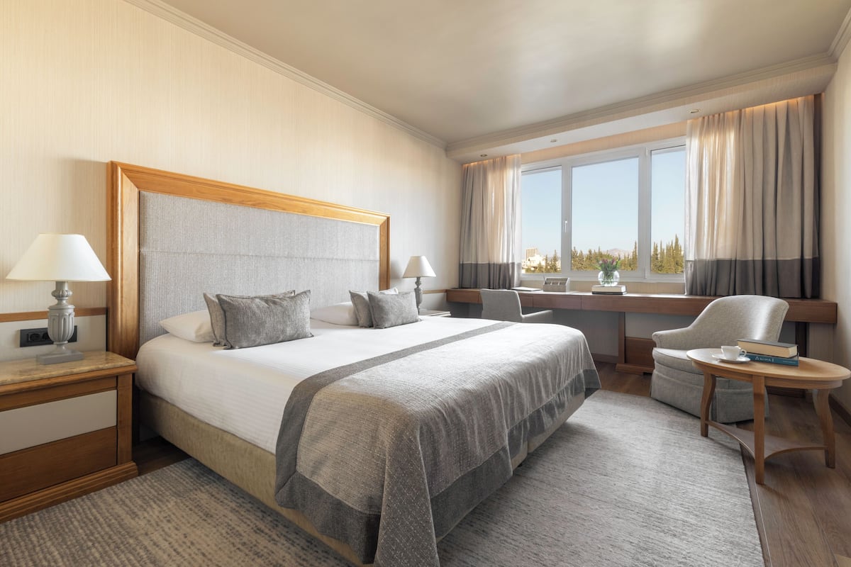 A hotel room with a large bed, a desk, a chair, and a view of the outdoors.