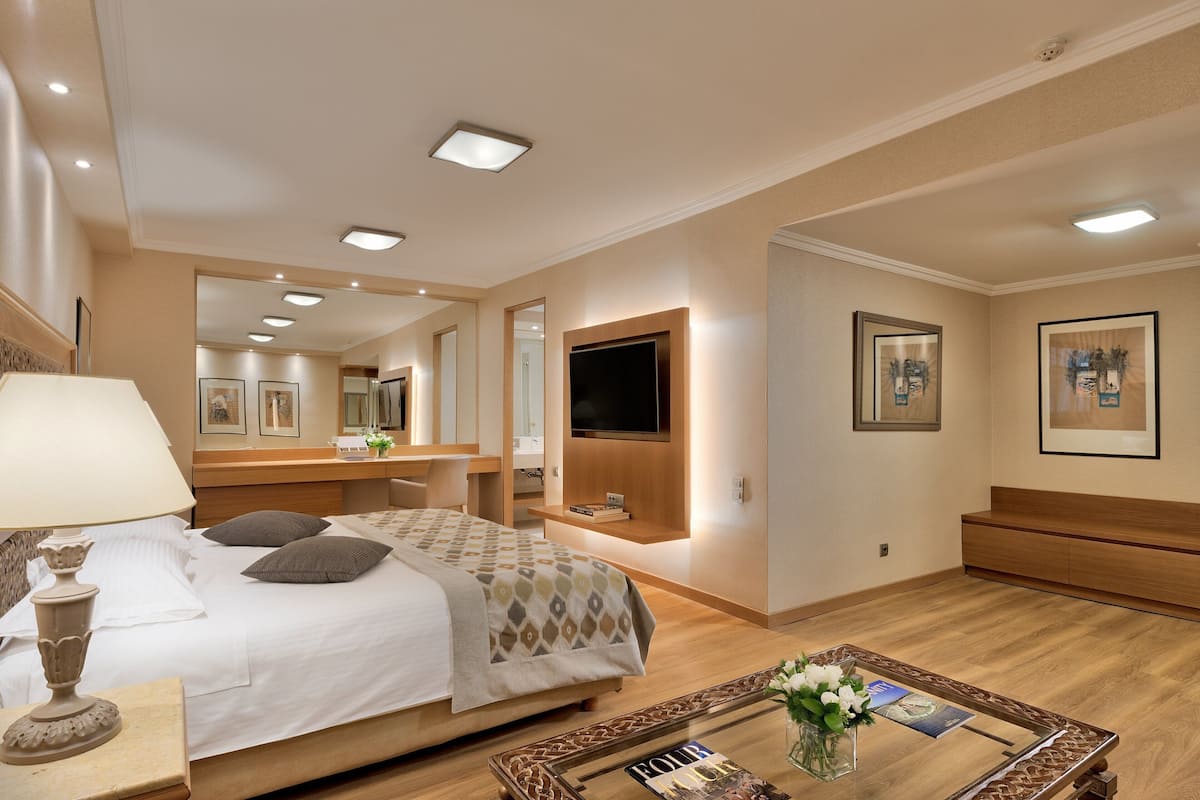 A hotel room with a bed, bedside table, lamp, TV, and a coffee table with a vase of flowers.