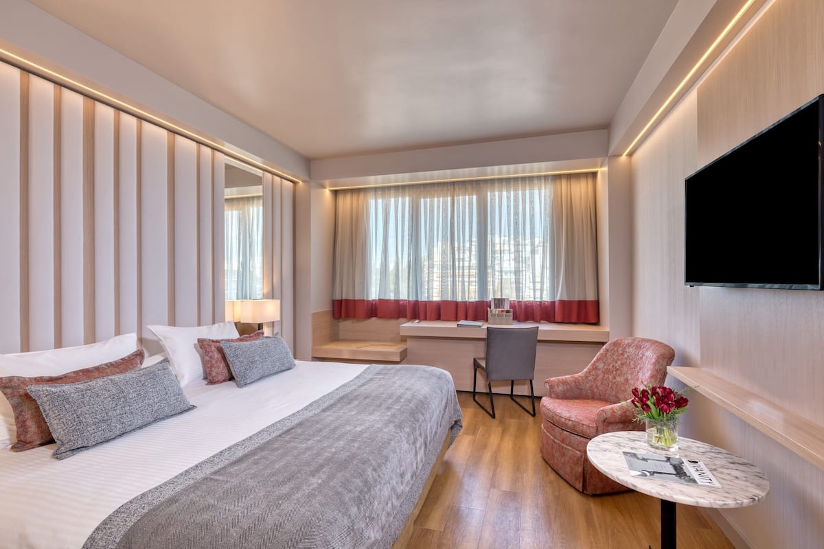 A hotel room with a bed, a desk, a chair, and a TV.