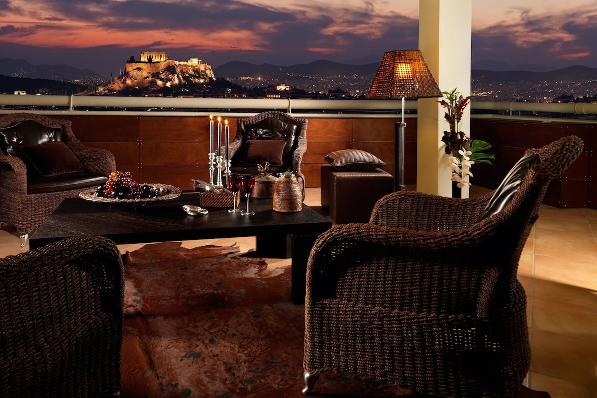 A balcony with wicker furniture, a table with candles, and a view of a cityscape at dusk.