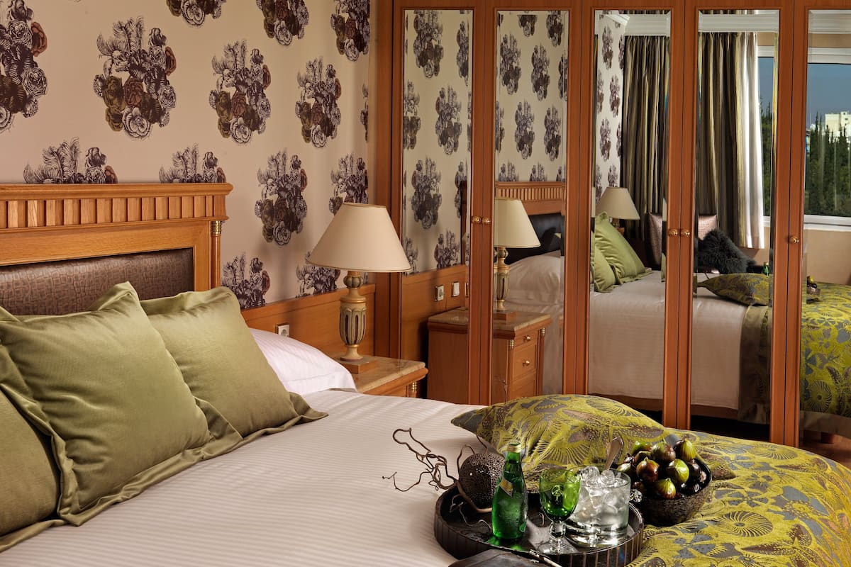 A hotel room with a bed, bedside table, lamp, and a mirror reflecting the room.