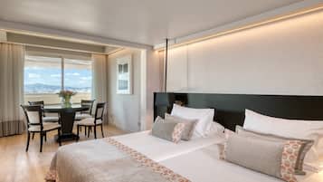 A hotel room with a large bed, a dining table with chairs, and a view of the mountains.