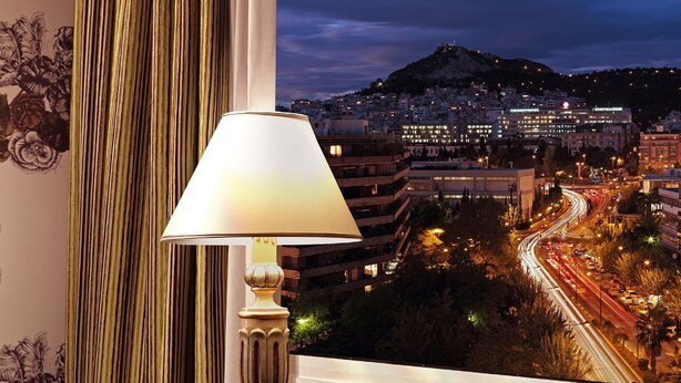 Une pièce avec vue sur une ville illuminée la nuit, comprenant une lampe, des sphères décoratives et des livres posés sur une table en verre.