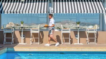 A poolside area with a view of a cityscape, including a historic building. There are white chairs and tables, and a person walking by.